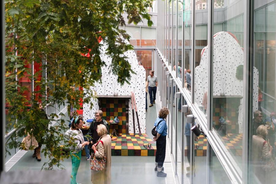 Mensen bekijken kleurrijke kunstinstallatie met schaakbordpatroon en wit decor met zwarte lijnen in het Atrium bij SCHUNCK met veel glas en een boom op de voorgrond.