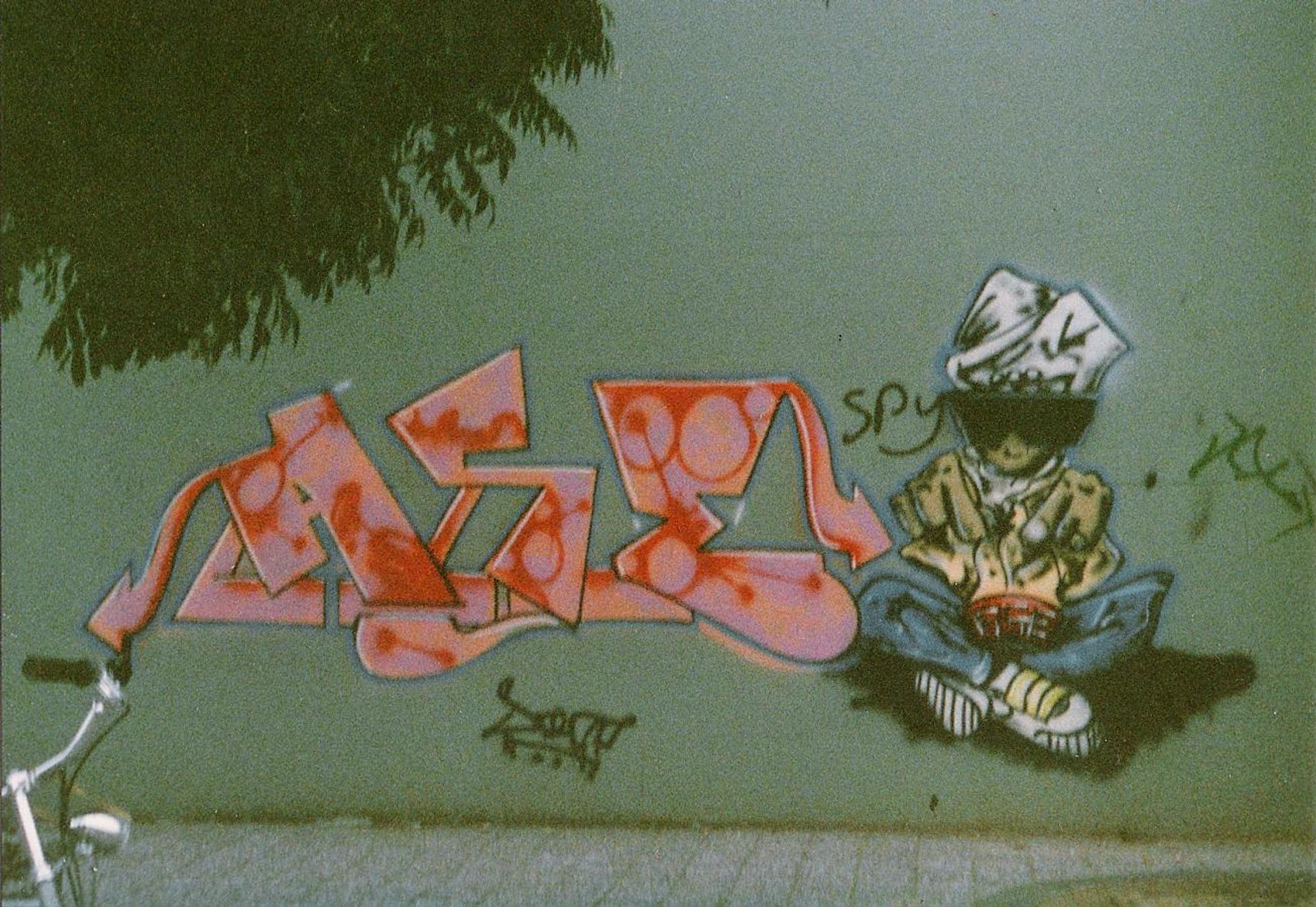 Graffiti op een muur met kleurrijke letters en een getekend figuurtje dat zittend een boek leest.