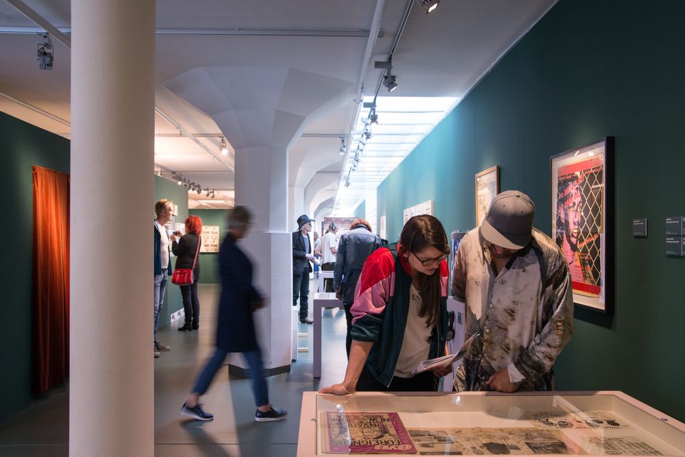 Bezoekers in museumzaal lopen en kijken naar kunst van Basquiat aan de wand en in vitrines. 