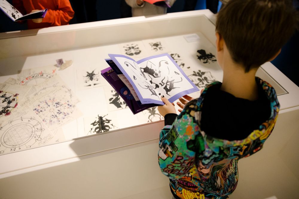 Kinderen staan naast vitrine van Andy Warhol met museum doe-boekjes in hun handen. 