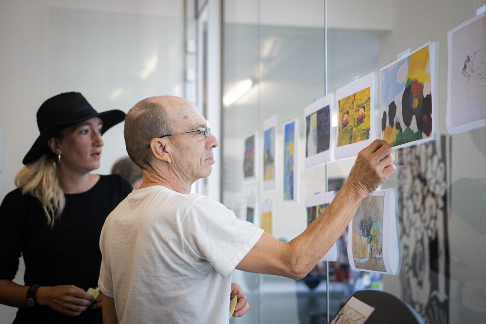 Een man bekijkt een selectie geprinte kunstwerken die op een glazen wand zijn geplakt.