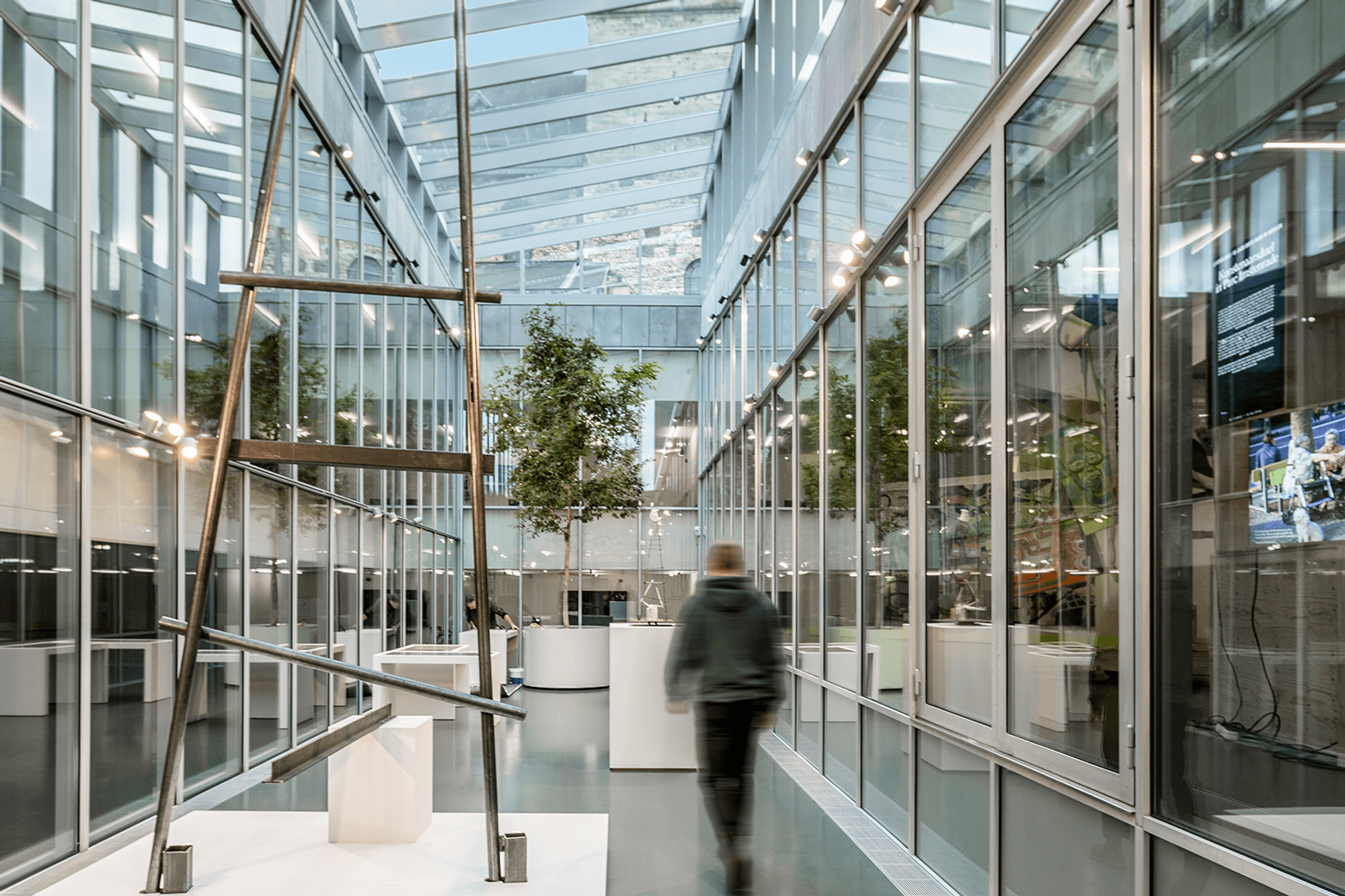 Interieur van het glazen atrium van het SCHUNCK Museum in Heerlen, gezien vanuit de andere kant. Op de voorgrond staat een ijzeren kunstwerk.