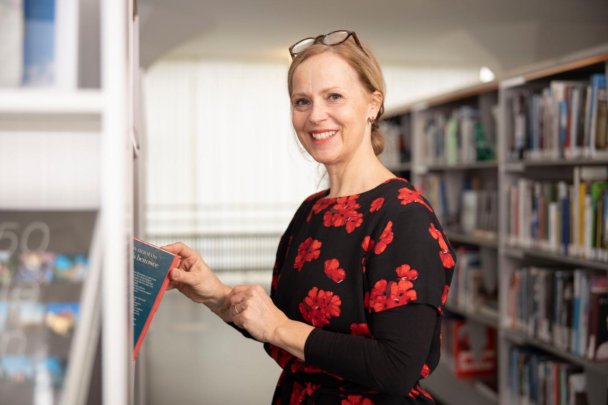 Gastvrouw Linda Wingen in bibliotheek staat bij de boekenkast en pakt een boek. 