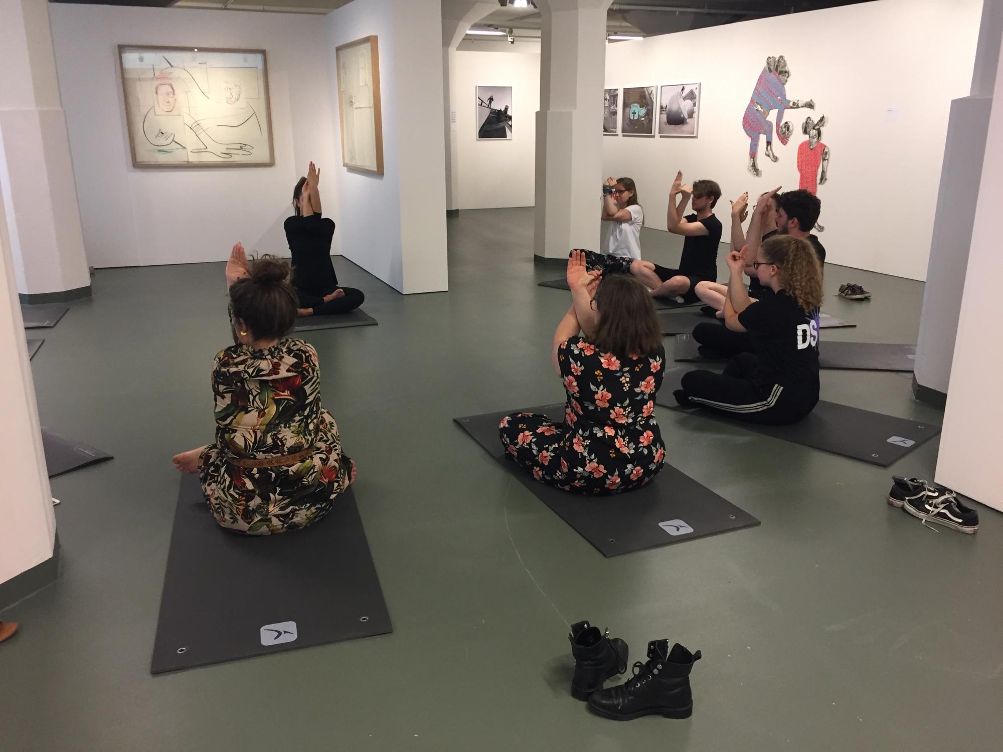 Groep mensen doet yogaoefeningen op matten tussen kunstwerken in een museumruimte tijdens een sessie van Museumgym bij SCHUNCK.