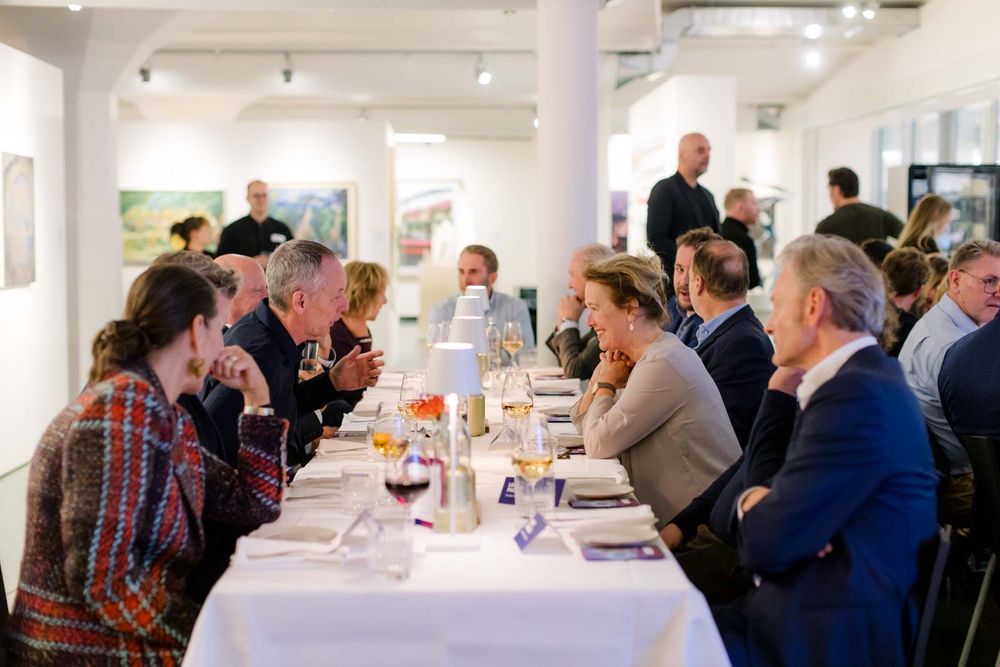 Mensen zitten en praten met elkaar aan een lange tafel in het museum. 