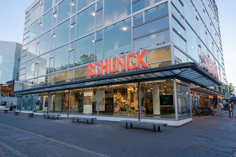 De glazen gevel van SCHUNCK met een presentatie van grote kunstwerken in de etalageruimte, zichtbaar vanaf het plein.