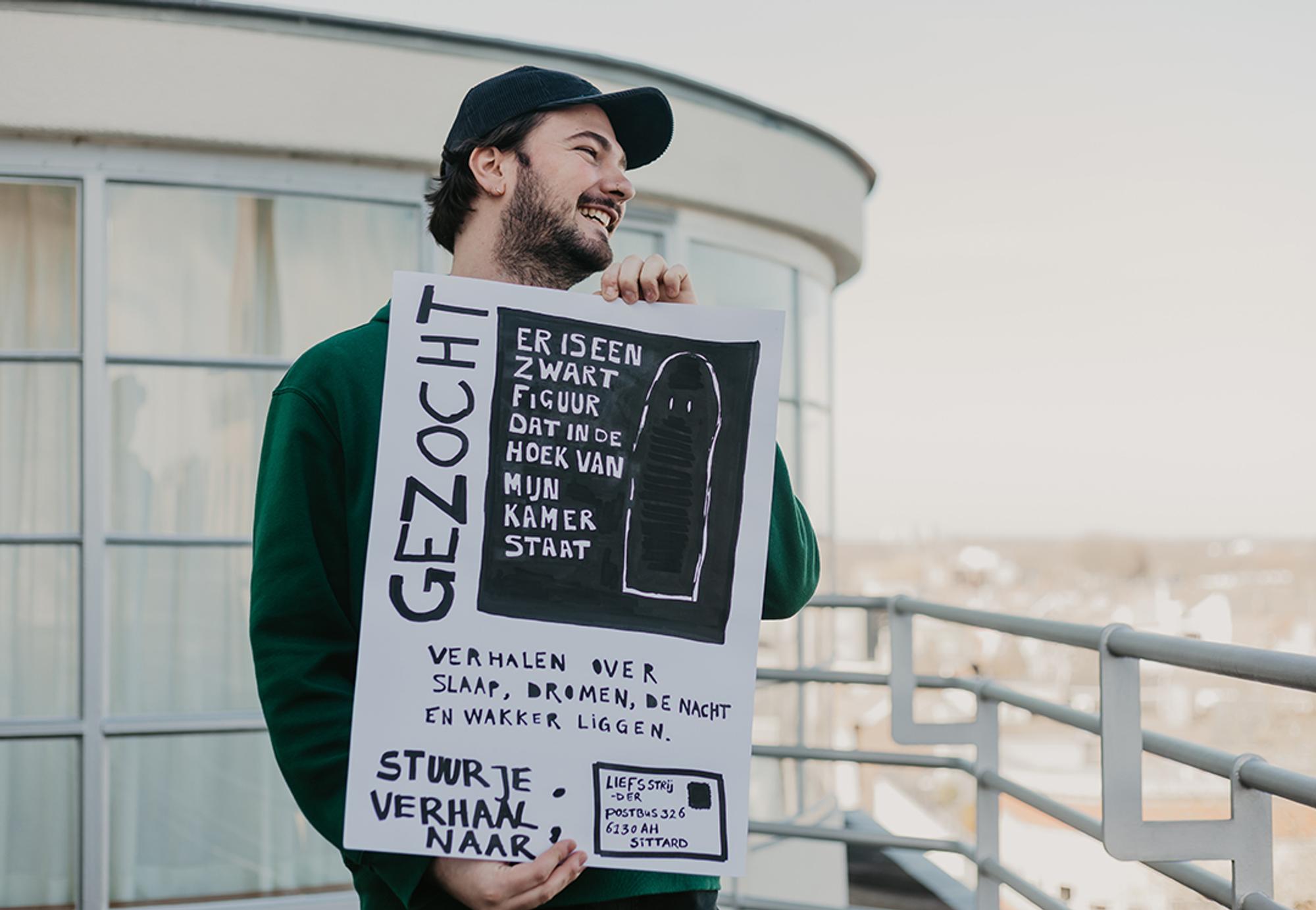 Portret van Boris Dieleman op het dak van SCHUNCK. In zijn handen houdt hij een poster met de tekst: 'GEZOCHT, er is een zwart figuur dat in de hoek van mijn kamer staat, verhalen over slaap, dromen, de nacht en wakker liggen, stuur je verhaal naar: Liefsstrijder postbus 326 6130AH Sittard.'