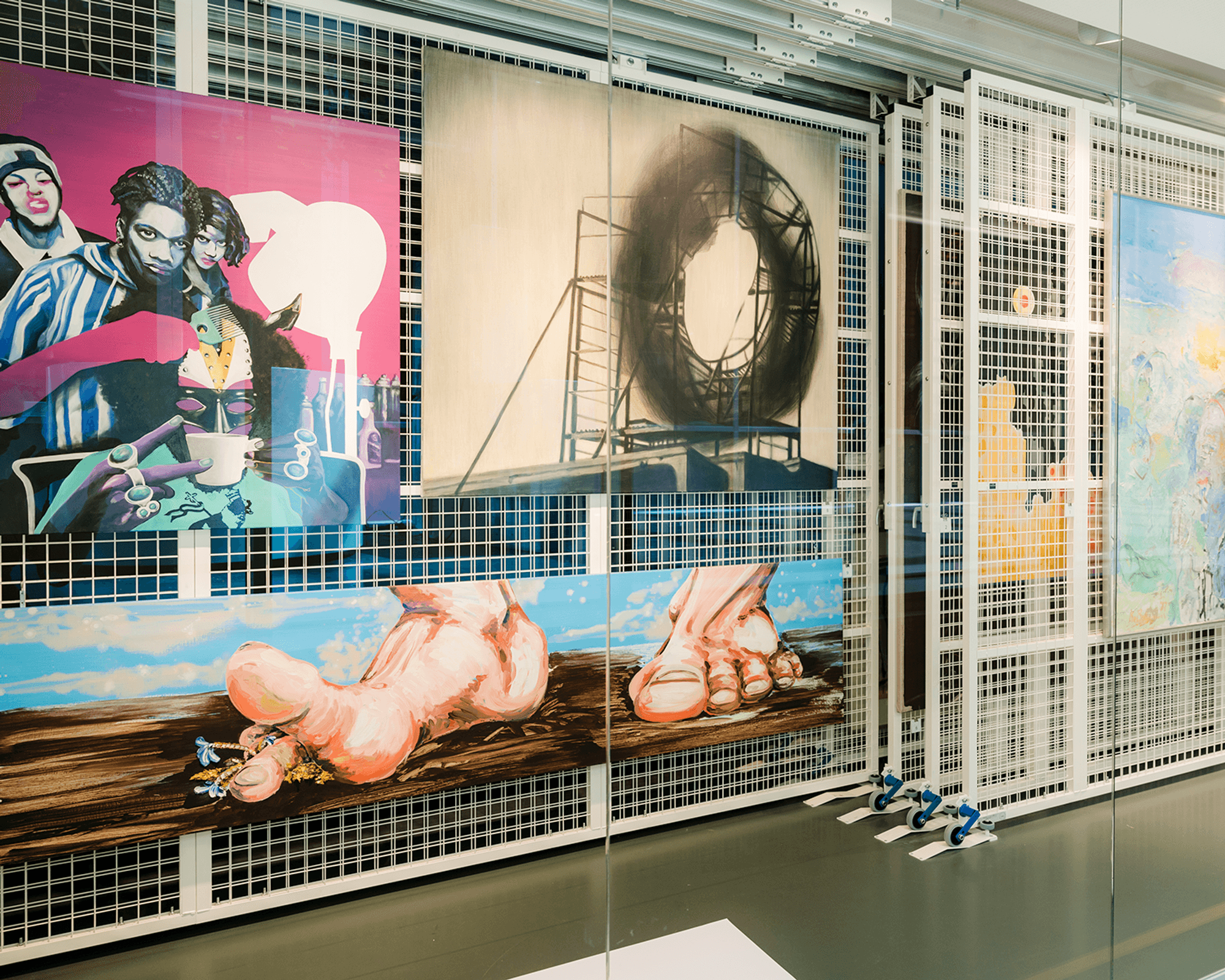 Uitschuifbaar rek in het kunstdepot met drie schilderijen: linksboven een werk met vier figuren op een roze achtergrond, rechtsboven een schilderij van een steiger met cirkel, en onderin een schilderij met twee voeten.