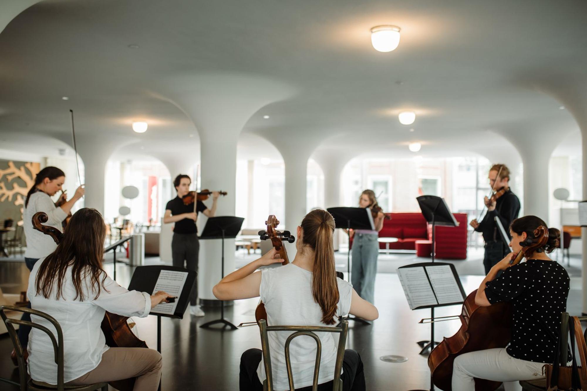 Zeven strijkers in een cirkelopstelling maken samen muziek op een verdieping bij SCHUNCK.