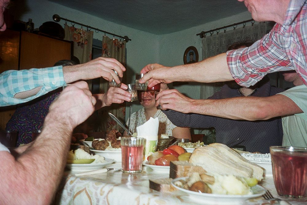Fotografie 'At the Mines' van Bertien van Manen (1994), Apanas, Siberië. Een groep mensen eet aan tafel en proost met een borrel.