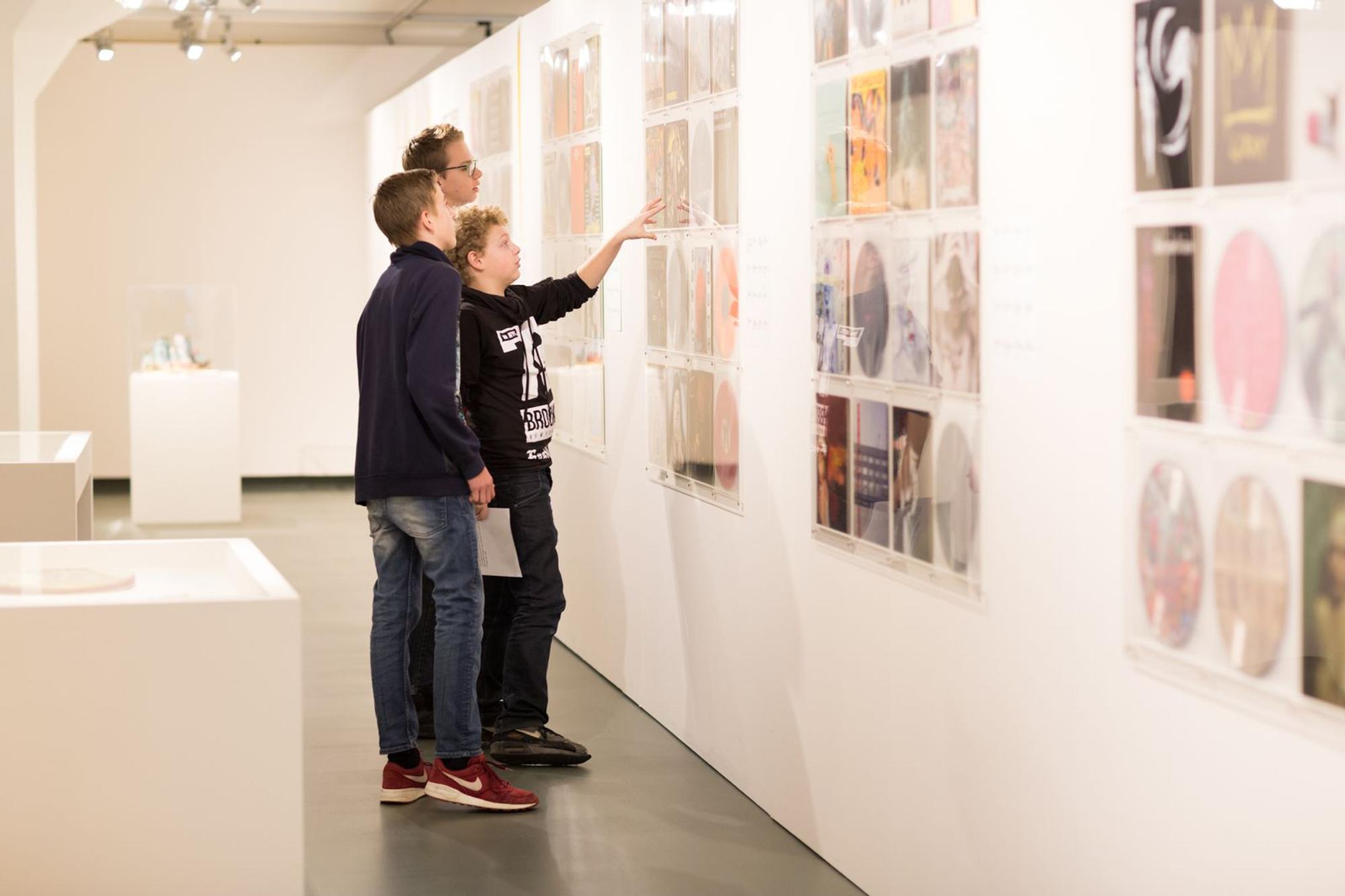 Drie jongeren in het museum wijzen naar foto's die aan de muur hangen. 