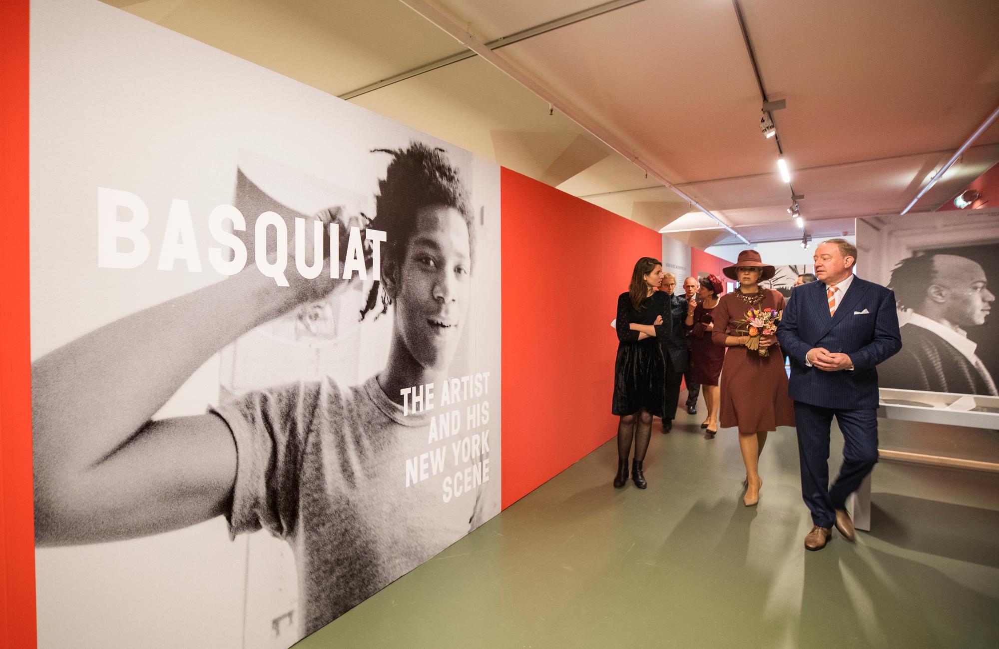 Koningin Máxima bezoekt de tentoonstelling "Basquiat: The Artist and His New York Scene" in SCHUNCK, terwijl ze door de gang loopt langs grote zwart-witportretten van de kunstenaar.