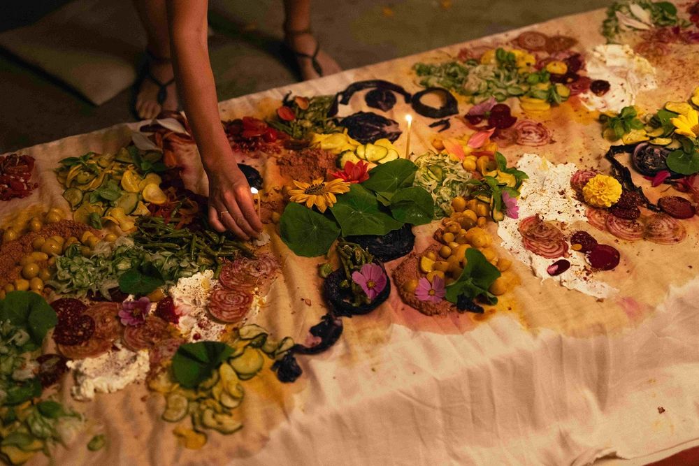 Tafel gedekt met wit tafelkleed, bloemen, eten en kaarsen. Performance Harvest Table Door Pleun Moons.