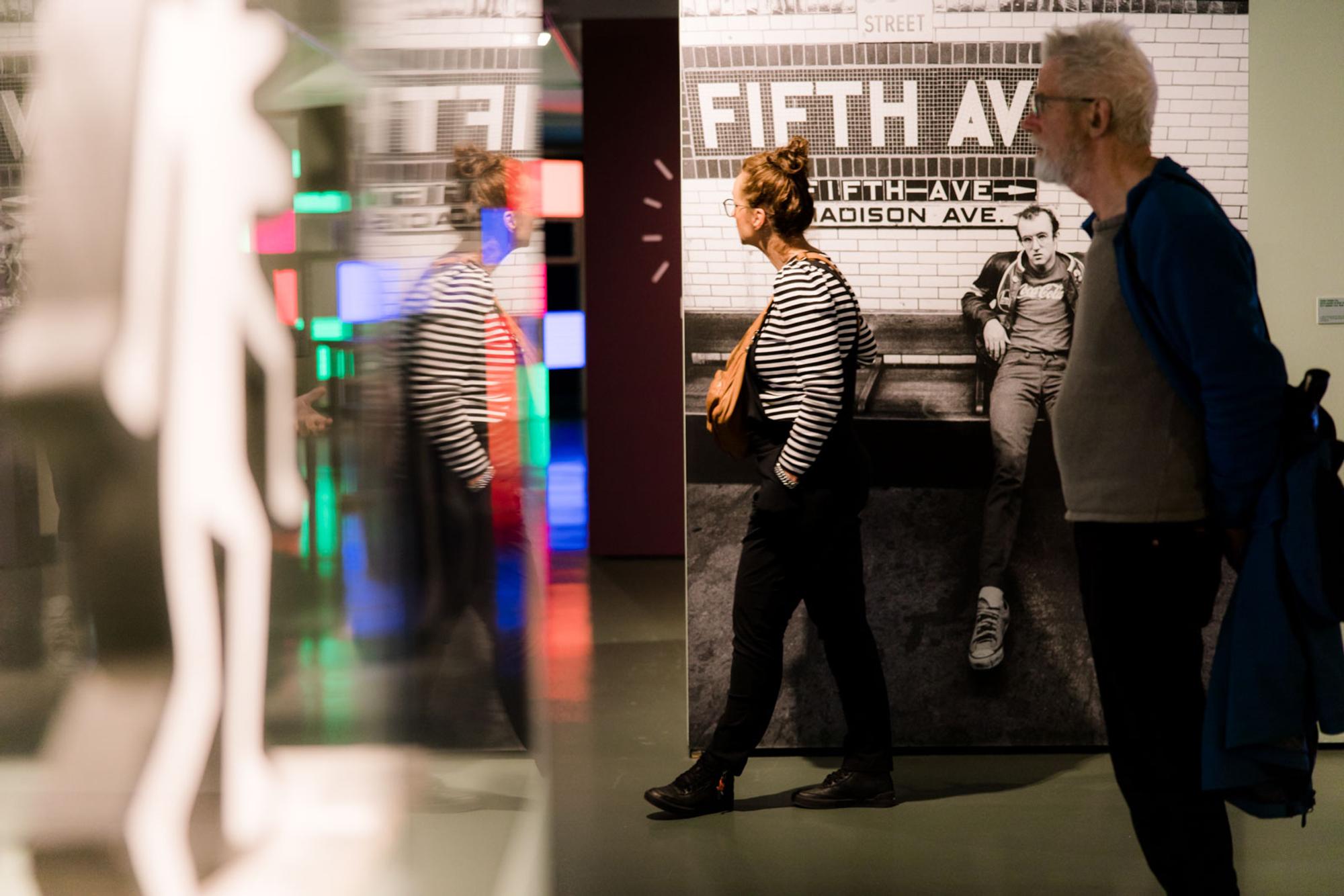 Twee bezoekers in het museum tijdens Keith Haring expositie. Sculptuur in glazen vitrine. 