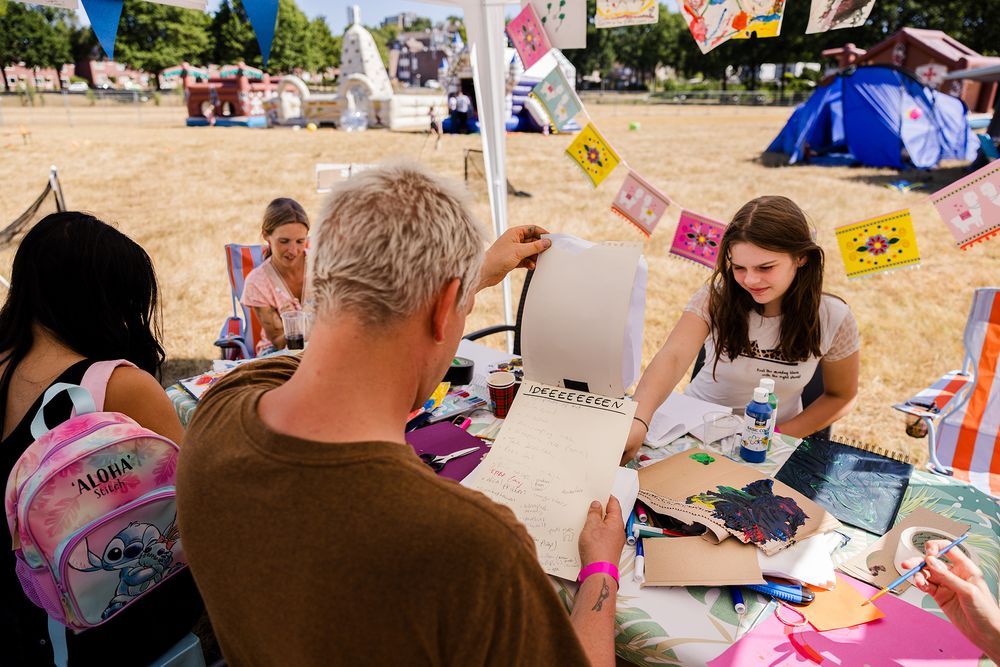 Maarten Bel bekijkt een vel met ideeën terwijl bewoners rond een tafel tekenen en schilderen op de Buurtcamping.