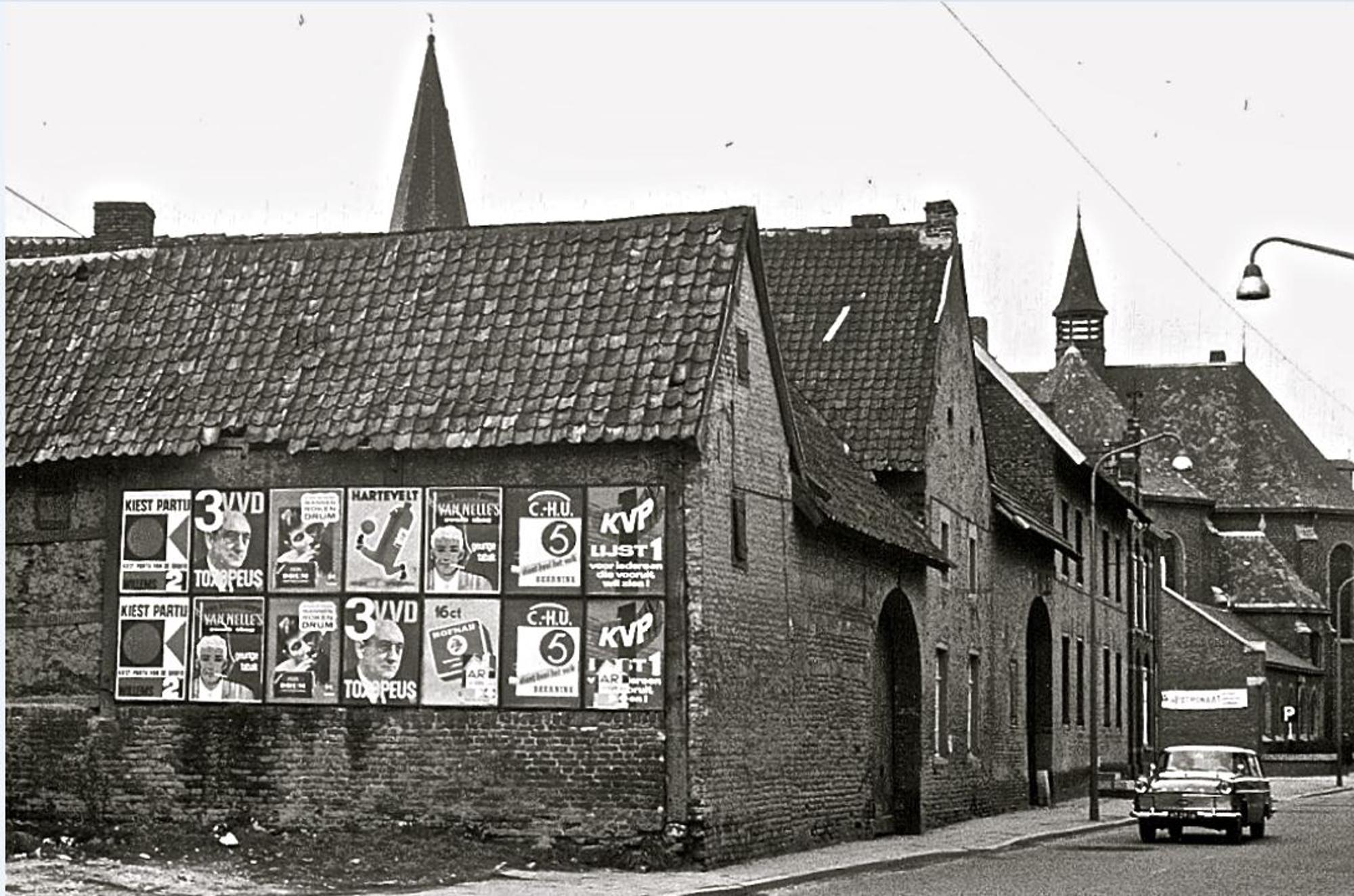 Een zwartwit foto van een oud straatbeeld. Op het eerste gebouw zijn wat politieke aanplakbiljetten geplakt. 