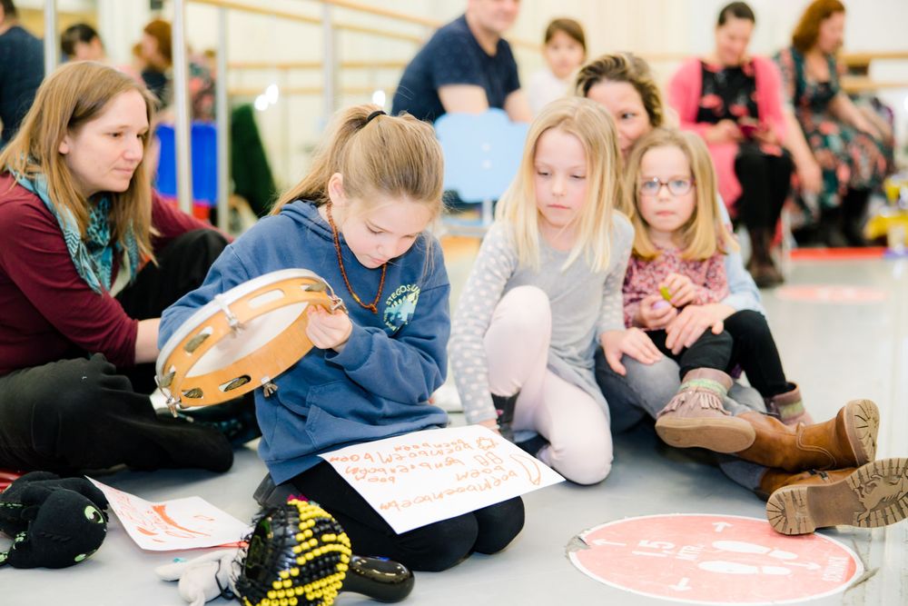 Kinderen zitten op de grond, een meisje houdt een tamboerijn vast.