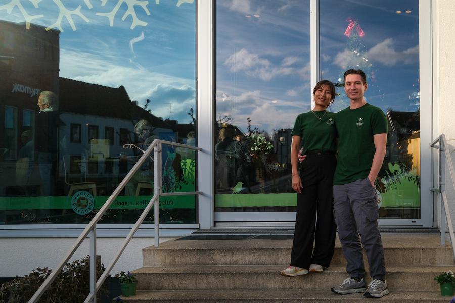 Jasper Sirre en zijn vrouw voor de ingang van Bagels & Beans Heerlen, bij de trap van het Glaspaleis, in groene bedrijfskleding.