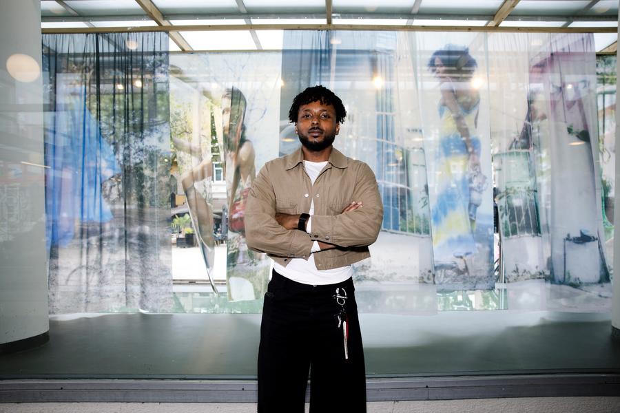 Beeldend kunstenaar Kevin Osepa voor zijn werk Beneath a Sacred Street in de vitrine van SCHUNCK Glaspaleis (2025). De installatie toont foto’s, doorschijnend textiel en objecten die verwijzen naar Afro-Caribische spiritualiteit en zijn geboortebuurt Domi Abou op Curaçao.