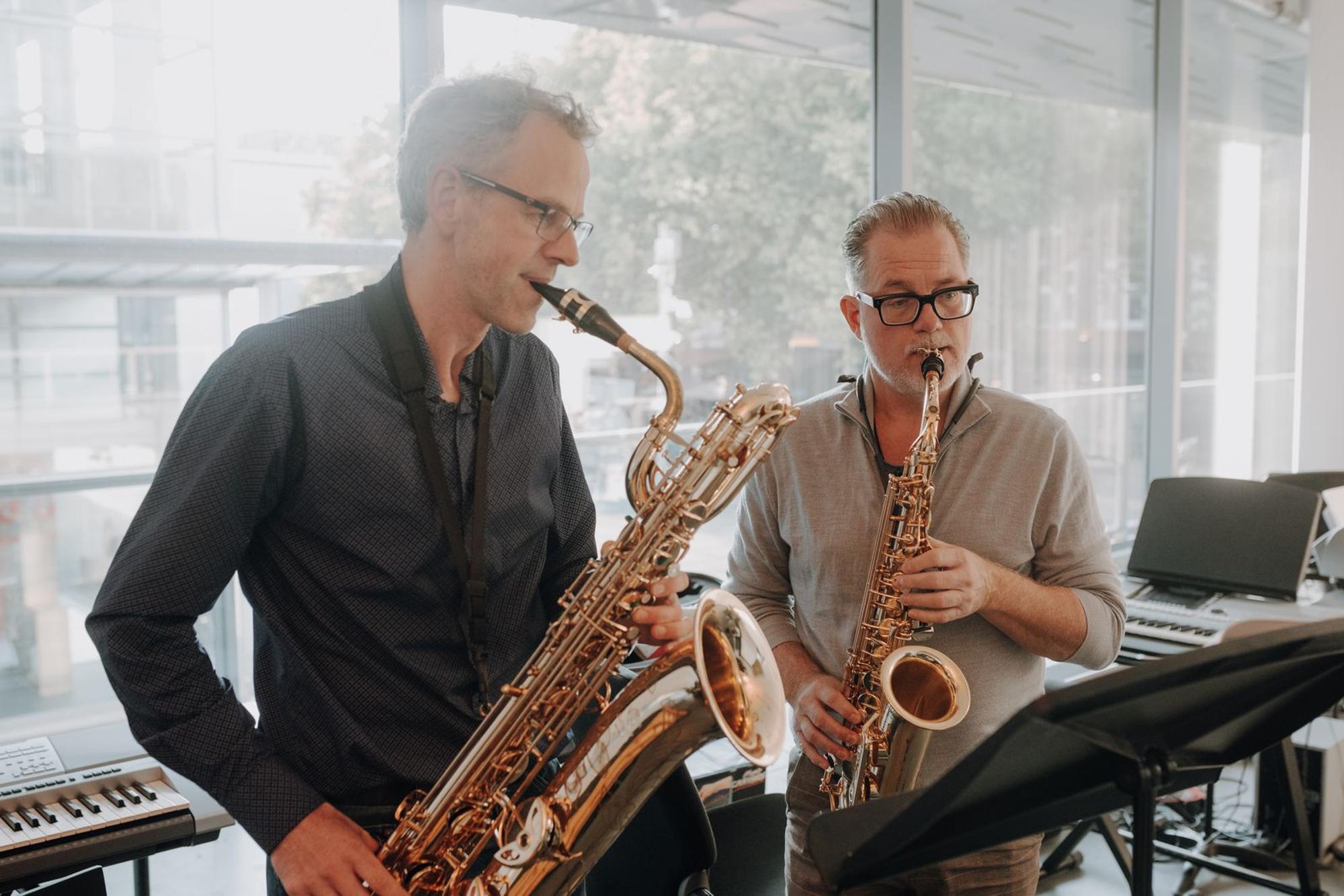 Leerling en leraar spelen samen saxofoon met piano's op de achtergrond. 
