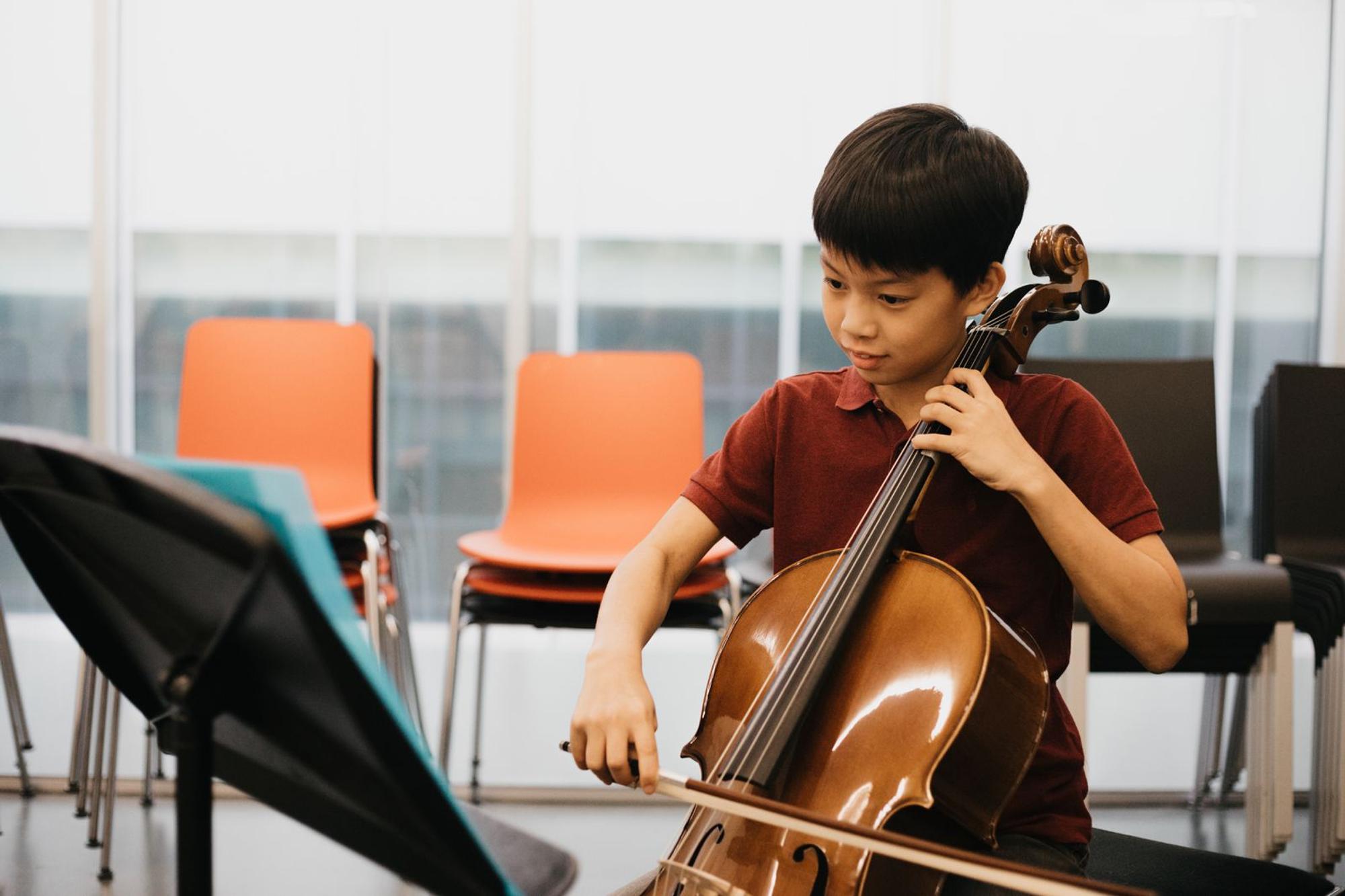 Jongen speelt cello, op de achtergrond staan lege stoelen.