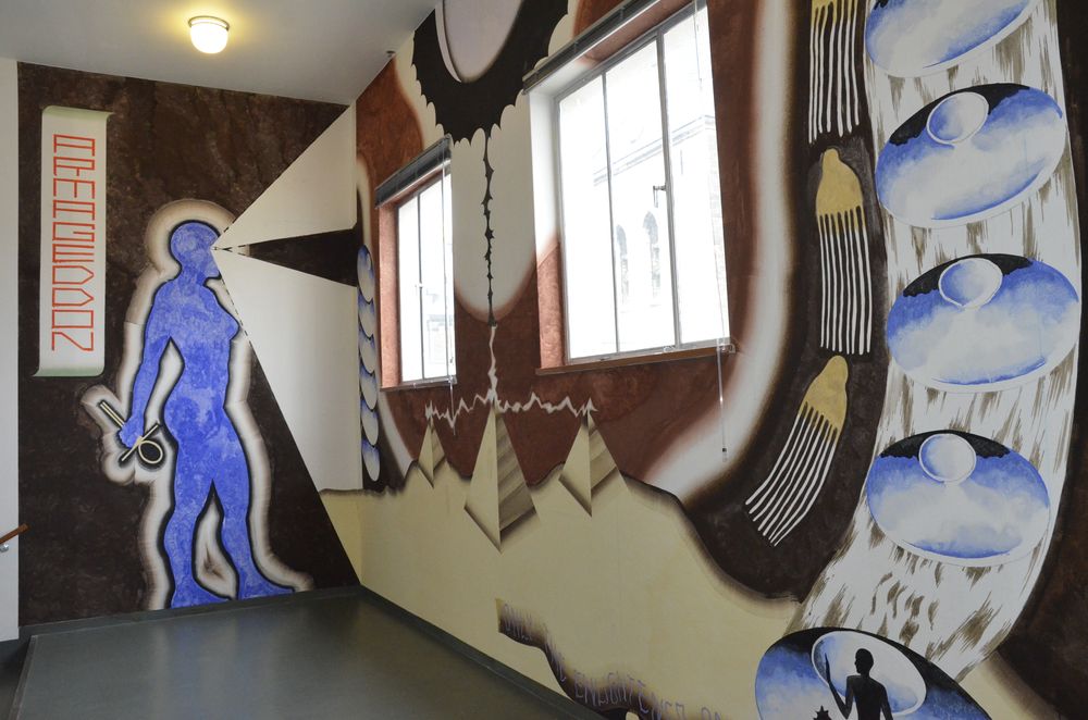 Muurschildering bij SCHUNCK van Fiona Lutjenhuis, met een blauwe menselijke figuur, het woord "ARMAGEDDON" en abstracte vormen en landschappen langs de muur.