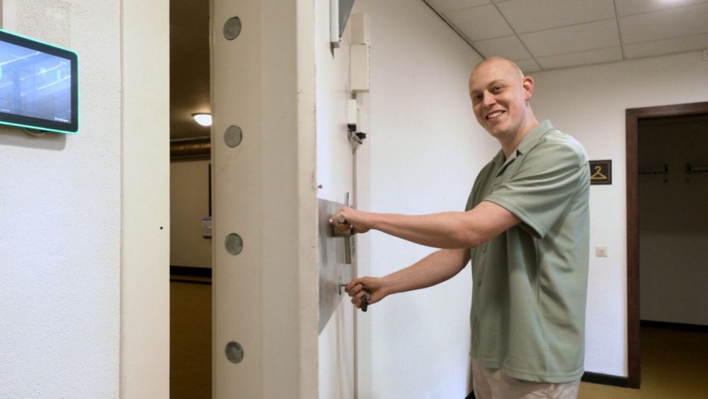Man opent een grote kluisdeur terwijl hij lachend in de camera kijkt.