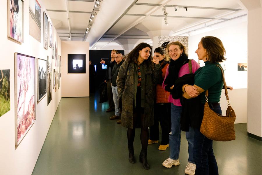 Groep mensen bekijkt kunstwerken aan de muur in een galerie of museumruimte met witte wanden en spotverlichting.