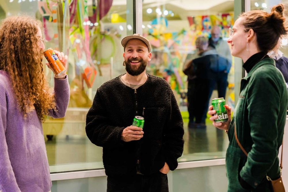 Drie bezoekers drinken uit blikjes en lachen met elkaar.