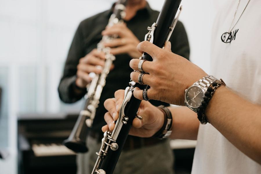 Close-up van een klarinet en twee handen die het vasthouden, met onscherp op de achtergrond nog een klarinettist.