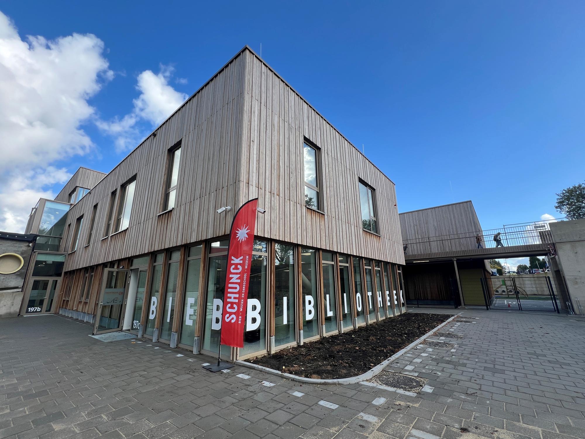 Buitenaanzicht van de SCHUNCK bibliotheek Heerlerbaan met houten gevel en rode vlag bij de ingang.