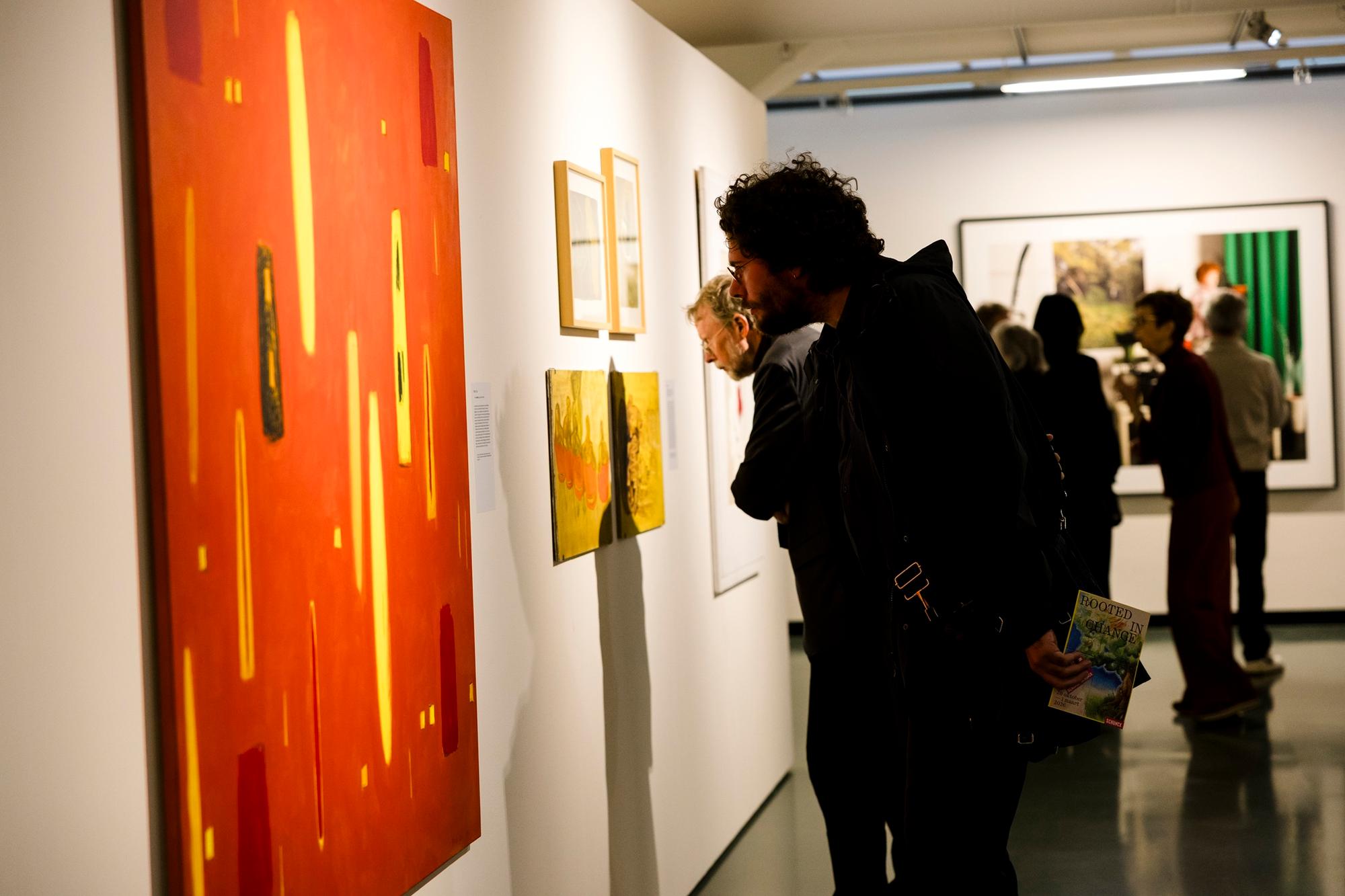 Bezoekers bekijken kleurrijke schilderijen in een kunstgalerie.