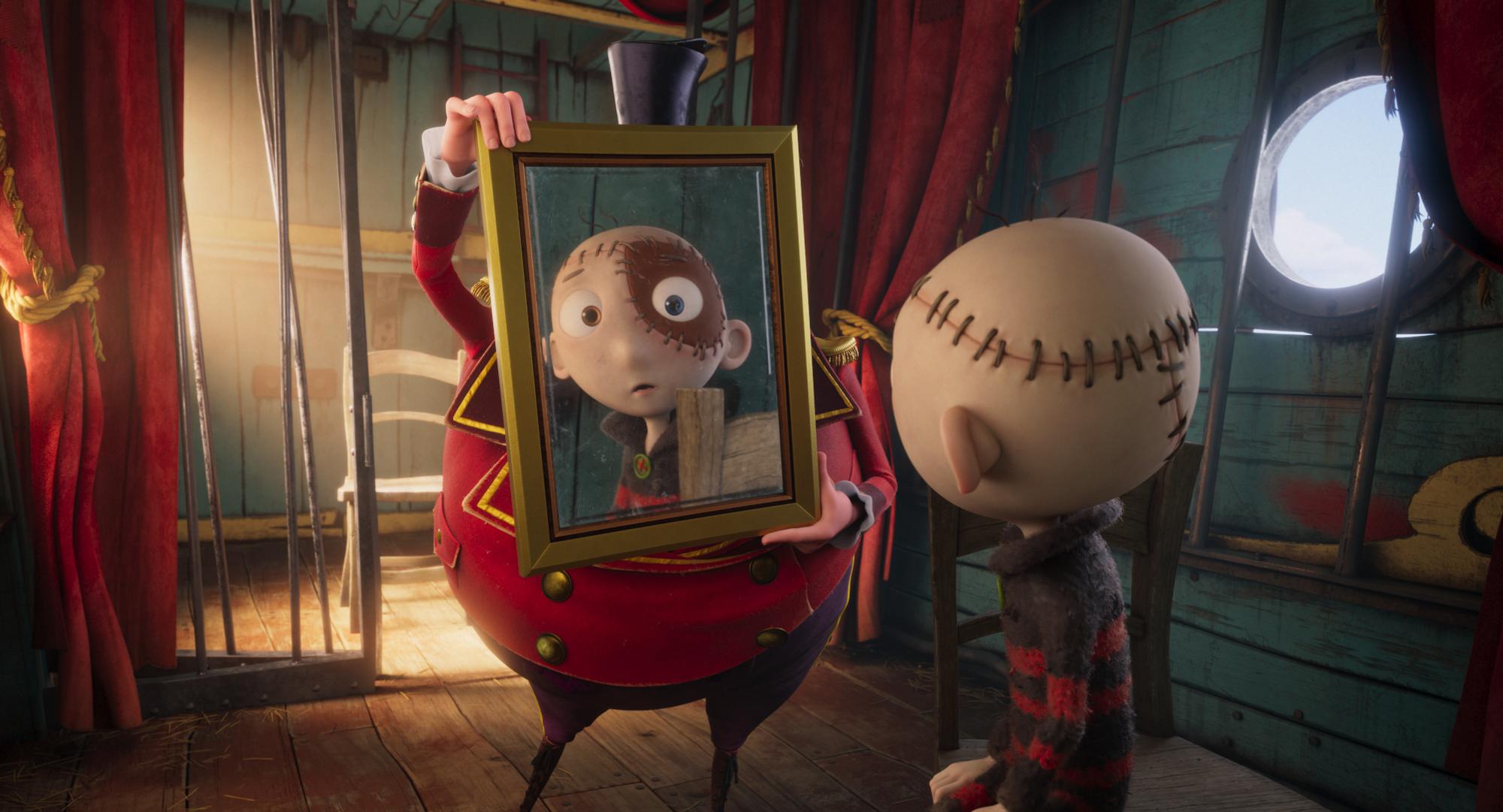 Beeld uit de animatiefilm 'Stitch Head': een figuur met zichtbare stiknaden op het hoofd staat in een houten kamer tegenover een ander personage dat een ingelijste spiegel vasthoudt. De warme belichting, rode gordijnen en fantasierijke vormgeving geven de scène een sprookjesachtige en mysteruze sfeer.