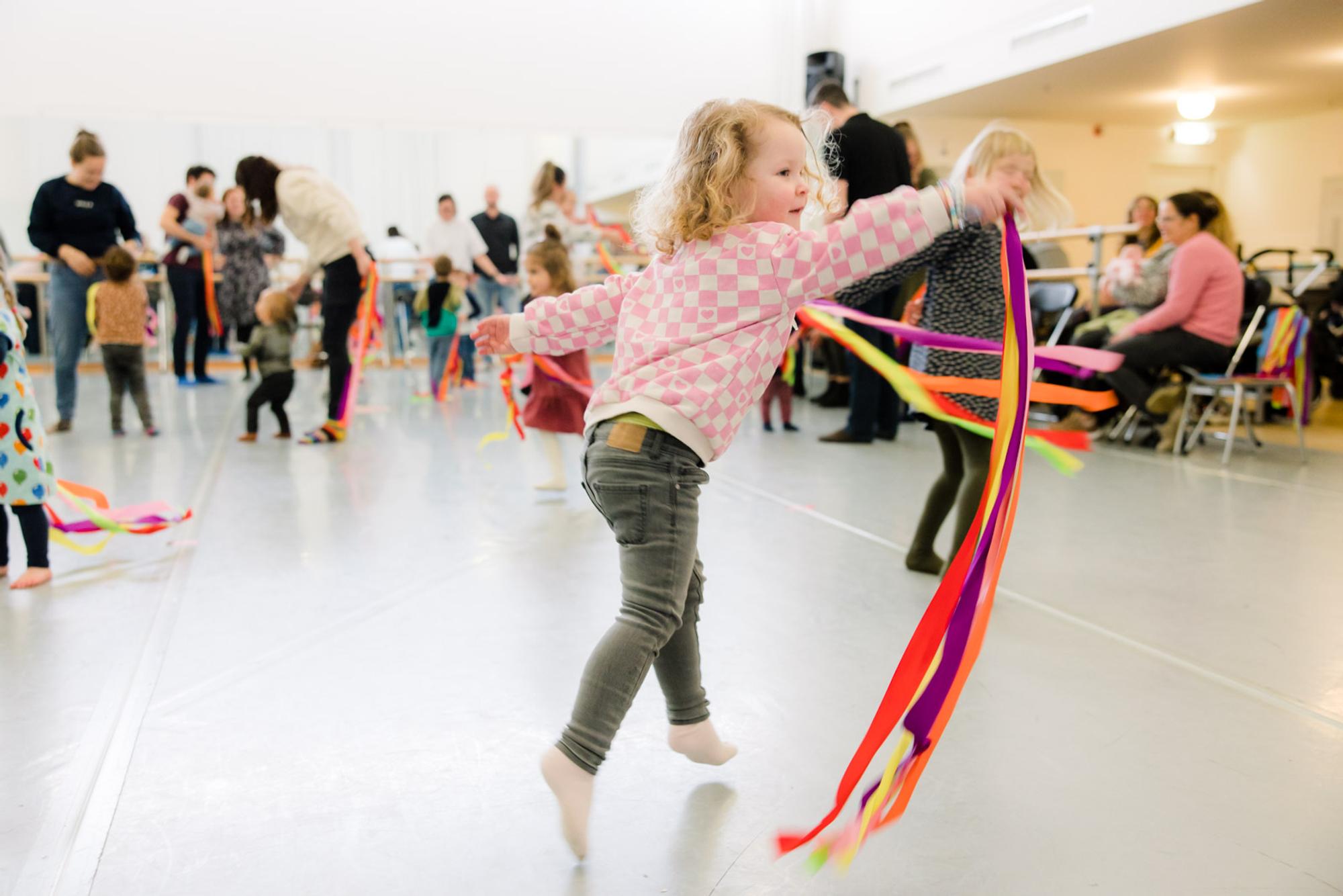 Kind danst met gekleurde lintjes in de danszaal van Schunck. 