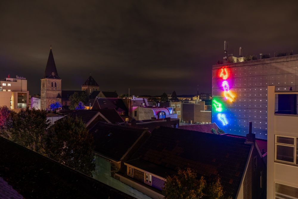 Nachtzicht over Heerlen met verlichte neonhanden op de gevel van de Plaarstraat.