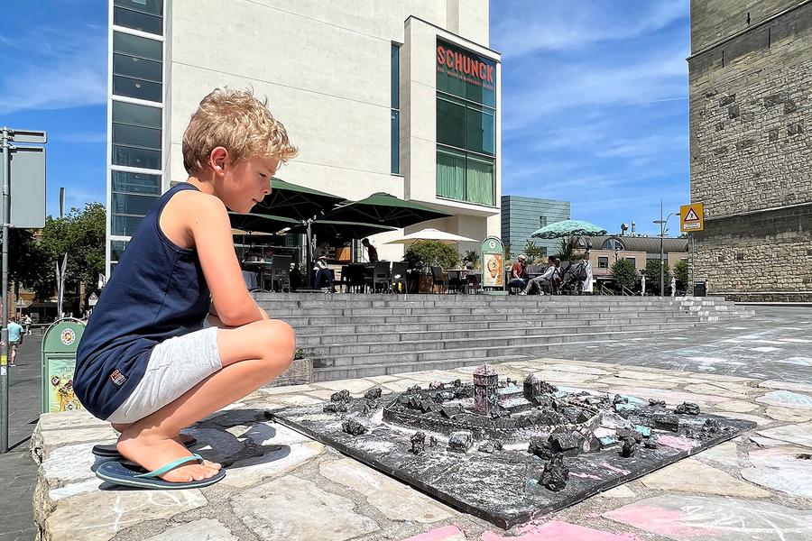 Kind zit buiten in de zon naast een maquette van Heerlen, voor het SCHUNCK Glaspaleis.
