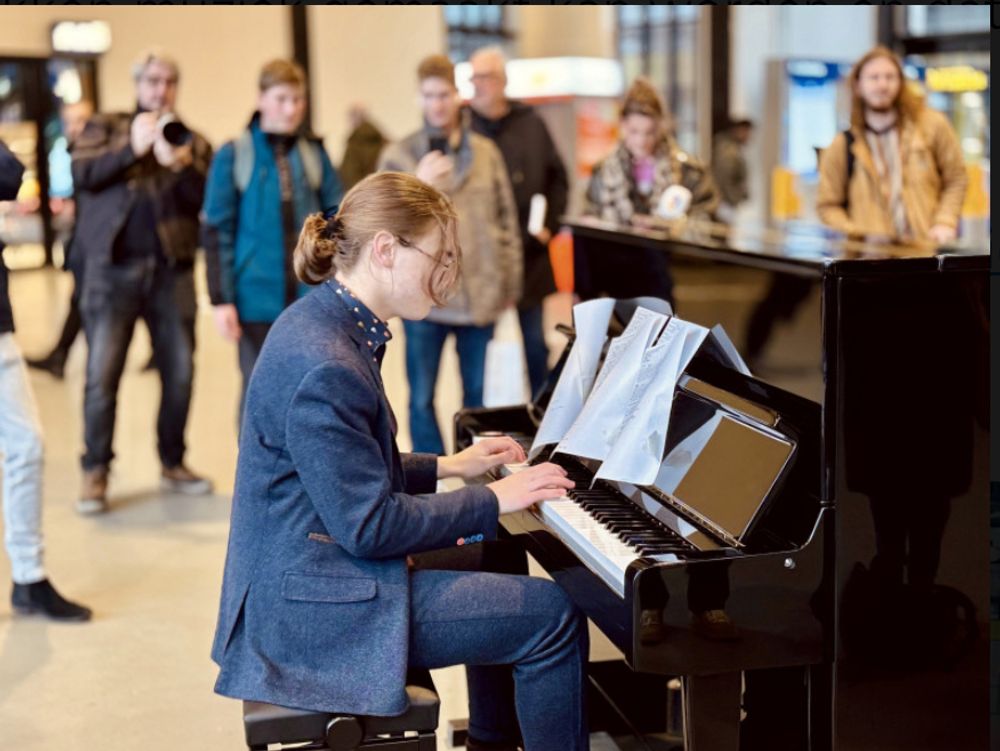 Jongen speelt piano in de stationshal van Heerlen. Op de achtergrond staan mensen te kijken. 
