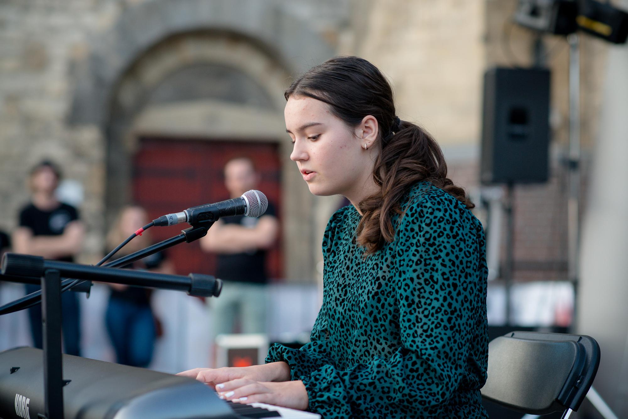 Meisje speelt piano en zingt tijdens een optreden buiten voor de Pancratiuskerk. 