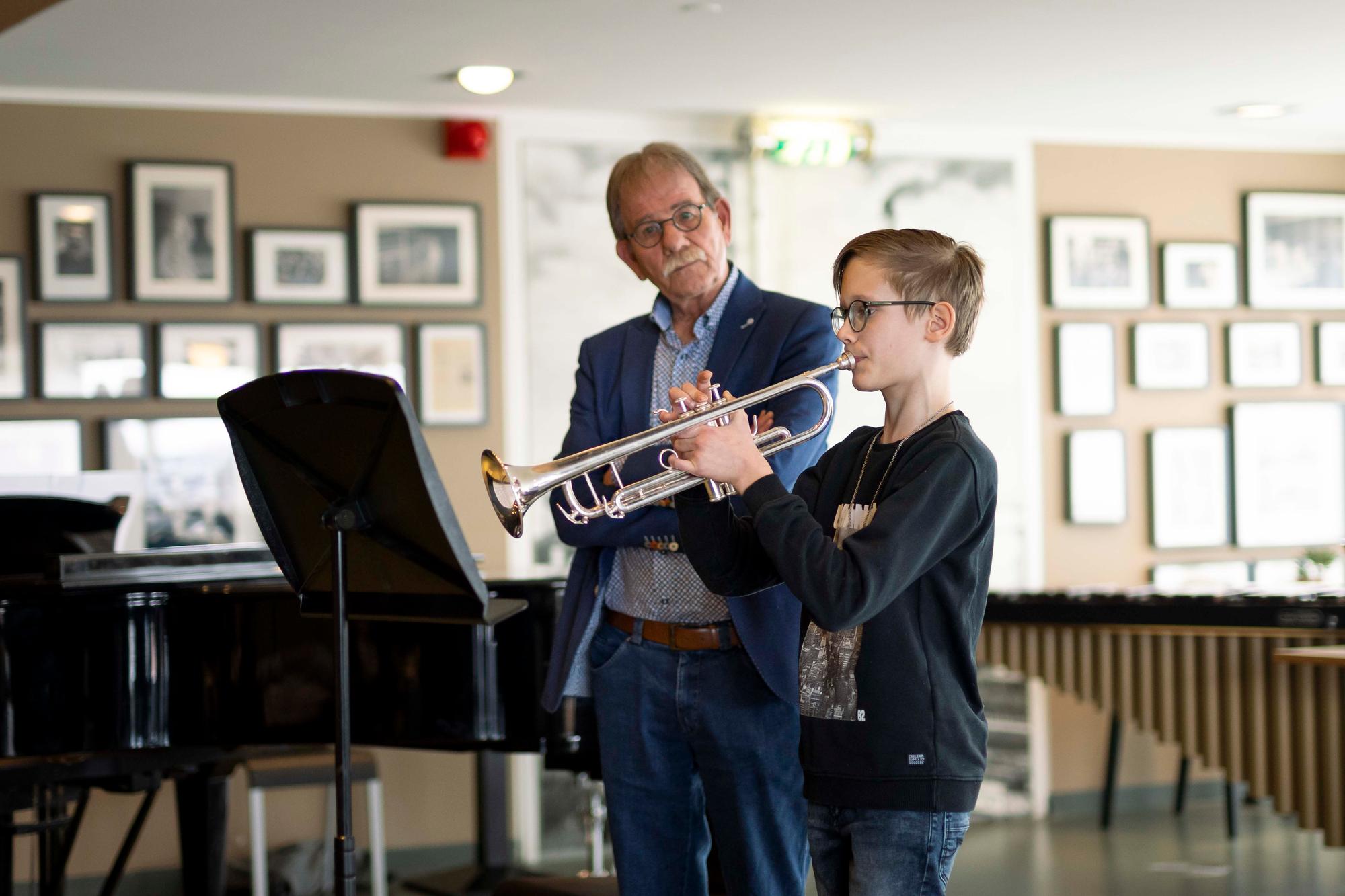 Leerling speelt trompet terwijl docent naast hem staat. 