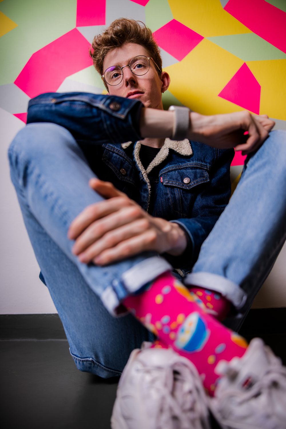 Portret van een jongeman die op de grond zit tegen een kleurrijke muurschildering.
