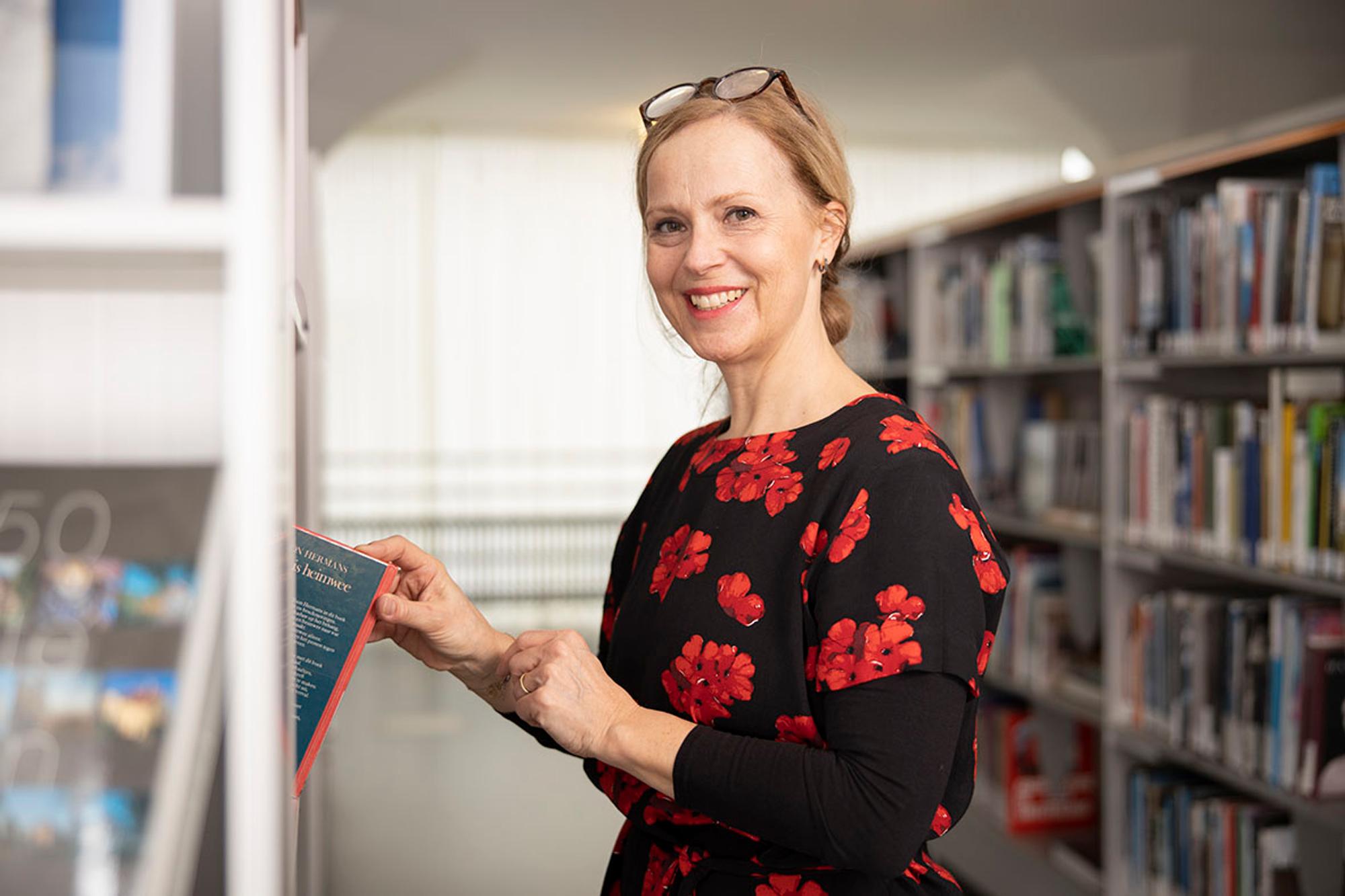 Portret  Linda Wingen, pakt boek uit kast. 