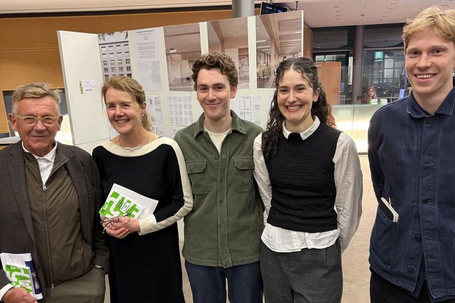 Groep van vijf mensen staat naast elkaar en glimlacht in een tentoonstellingsruimte met panelen op de achtergrond.