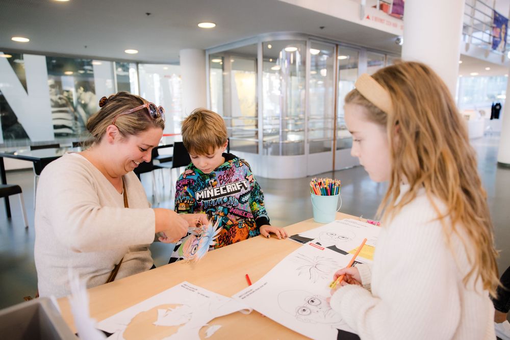 Twee kinderen en een vrouw knutselen in Andy Warhol thema aan een tafel in de centrale hal van Schunck. 