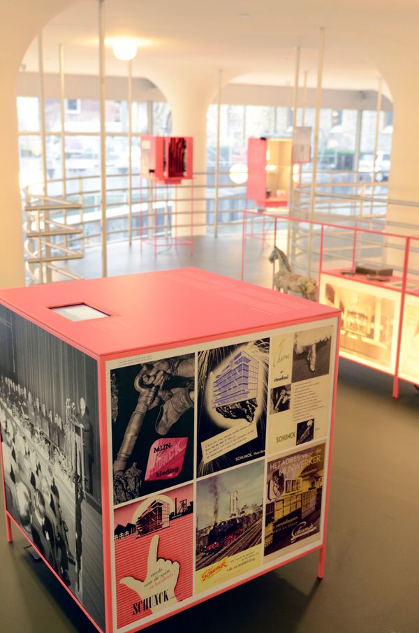 Overzicht van een expositie in SCHUNCK met rode vitrinekasten gevuld met historische foto's, affiches en objecten over de geschiedenis van het Glaspaleis.