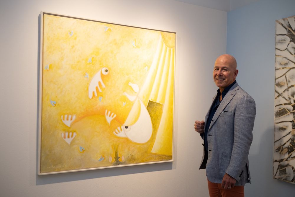 Een man kijkt naar de camera, met naast hem een abstract geel schilderij.