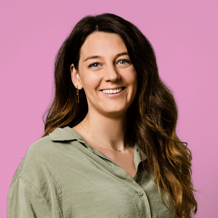 Portret van Gina met lang golvend haar en een lichtgroene blouse tegen een roze achtergrond.
