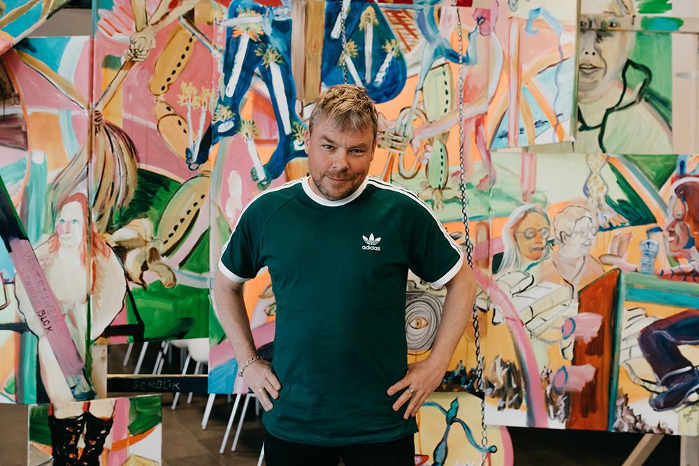 David Bade in groen Adidasshirt staat met zijn handen in zijn zij voor een kleurrijk schilderwerk.