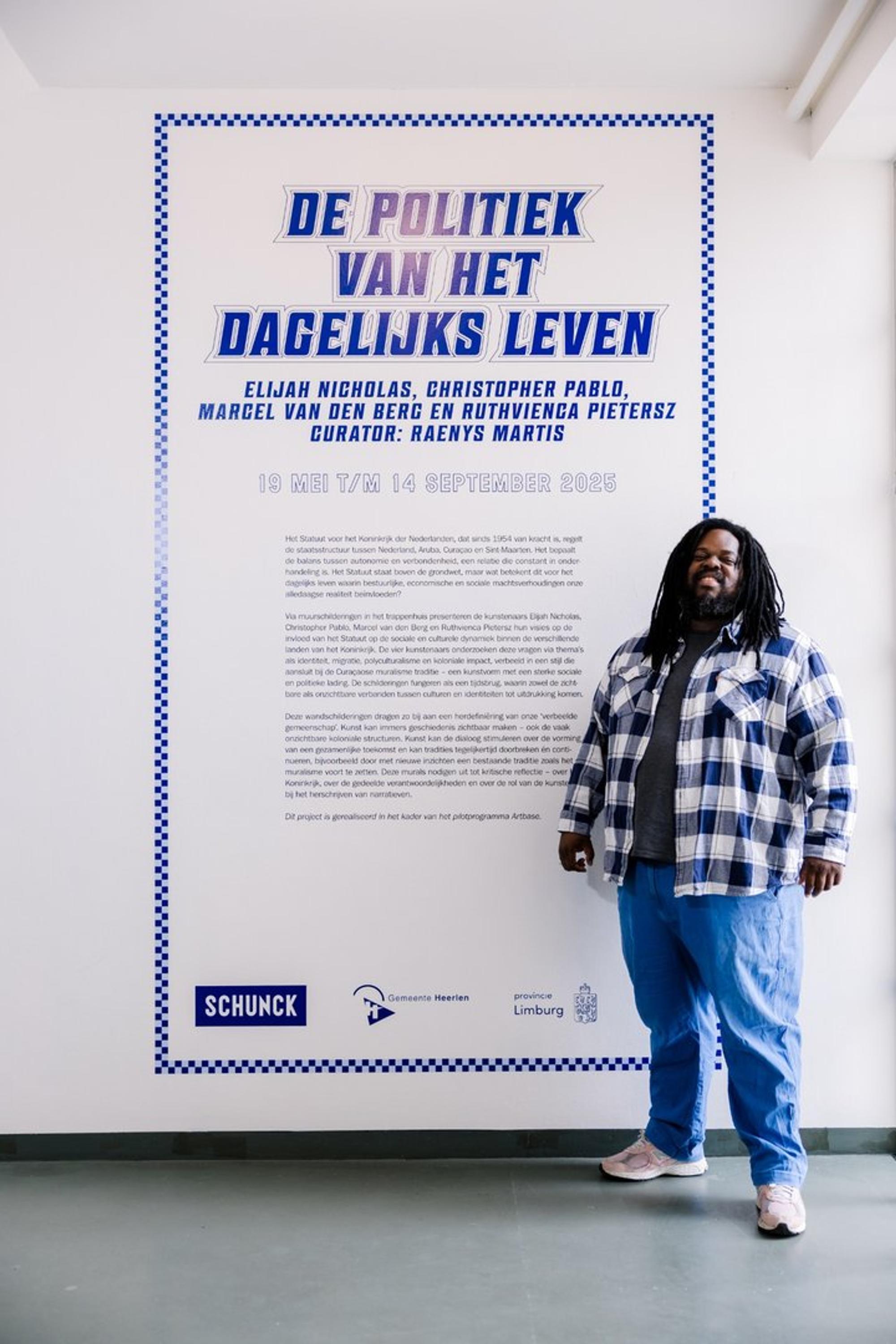 Curator Raenys Martis poseert bij de titelmuur van de tentoonstelling 'De Politiek van het Dagelijks Leven'.