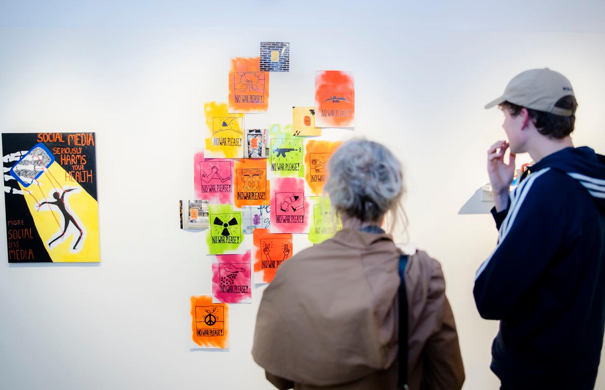 Keith En Ik Eindexamenexpo Twee bezoekers bekijken kleurrijke kunstwerken met sociale en politieke boodschappen tijdens de eindexamenexpositie ‘Keith en ik’ in SCHUNCK.