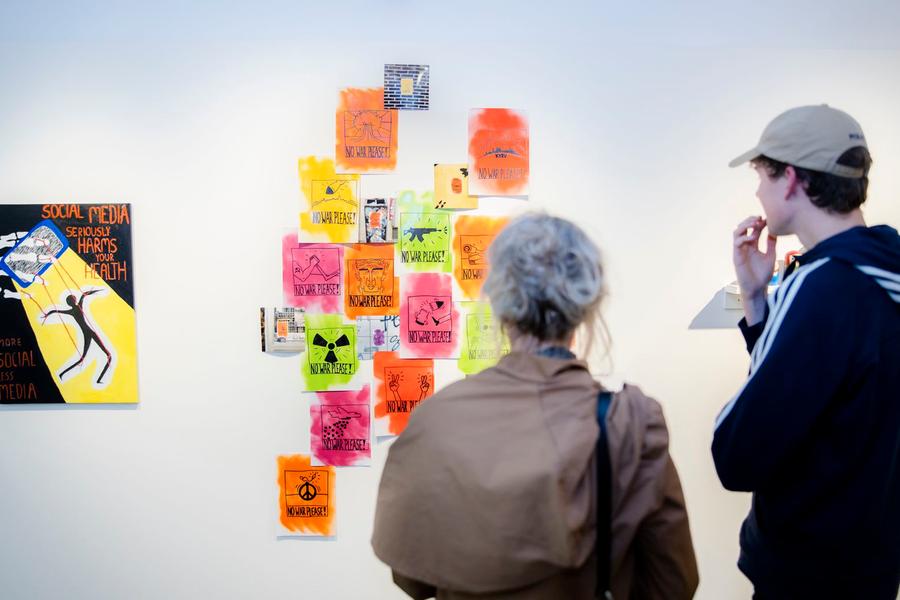 Twee bezoekers bekijken kleurrijke kunstwerken met sociale en politieke boodschappen tijdens de eindexamenexpositie ‘Keith en ik’ in SCHUNCK.